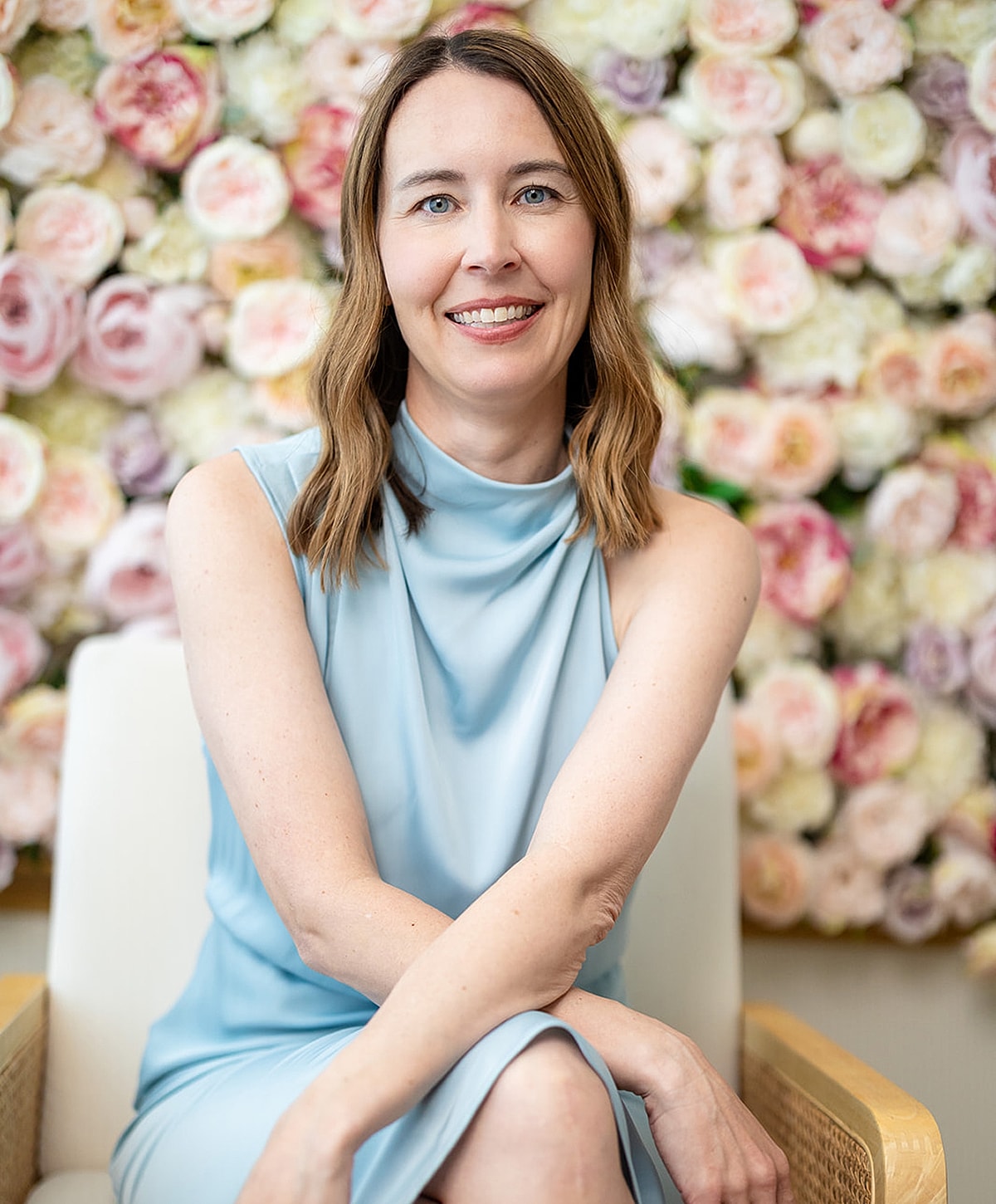 Woman in blue dress seated with floral background.