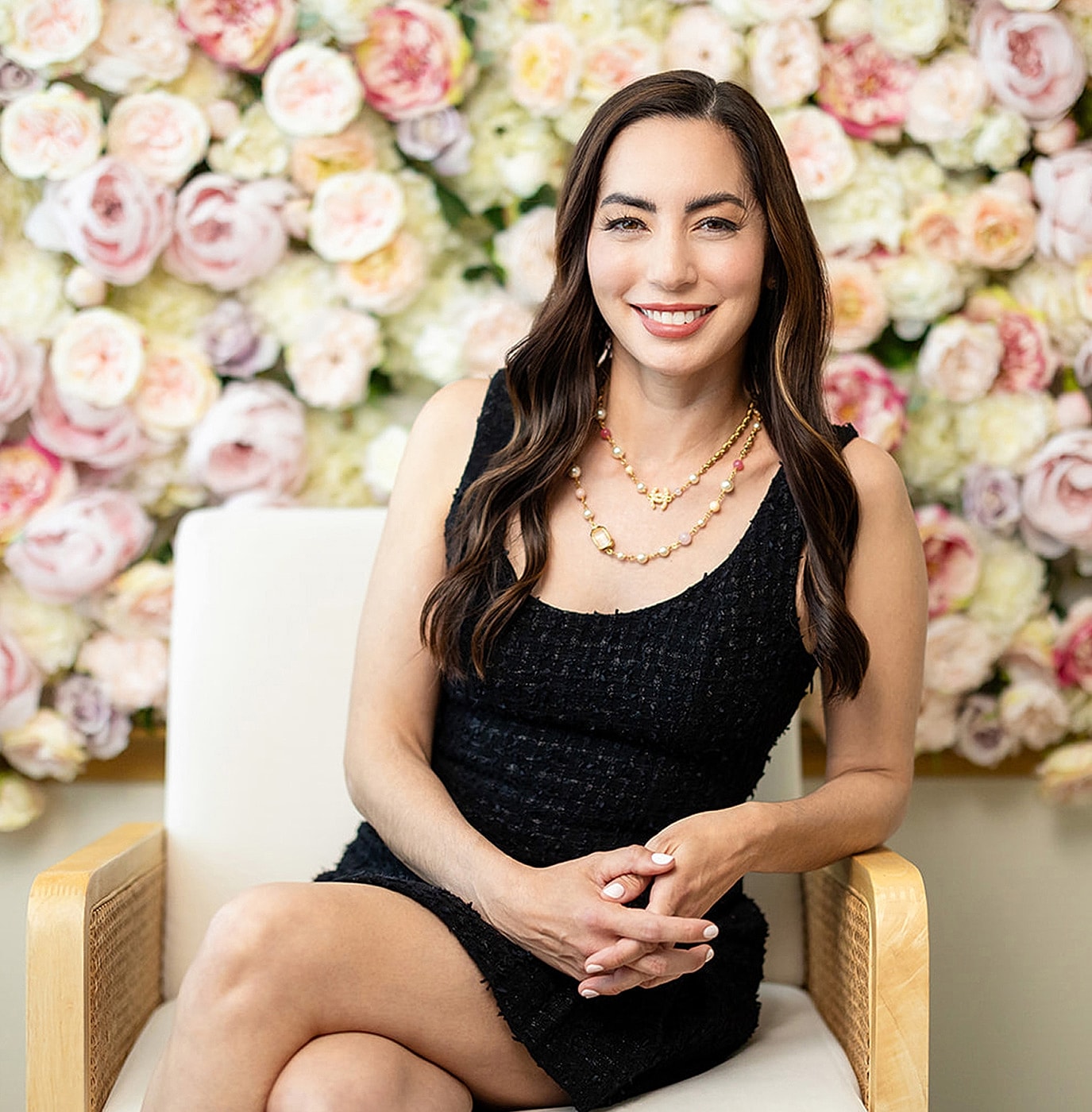 Woman in black dress smiling, floral background.