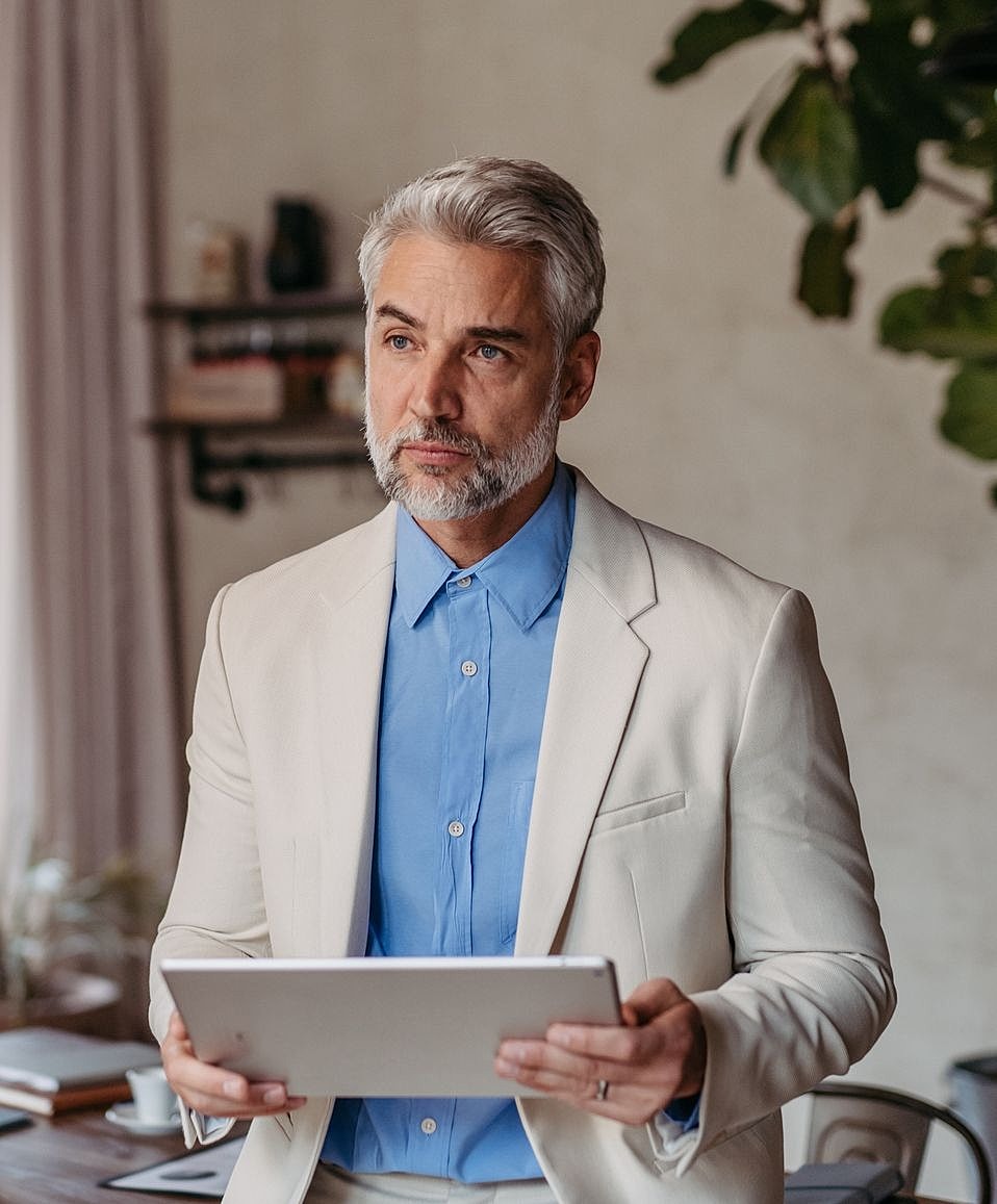 Man in suit holding tablet, thoughtful expression.