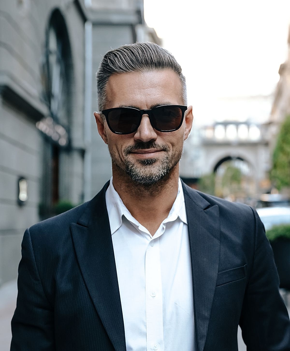 Man in sunglasses wearing a suit outdoors.