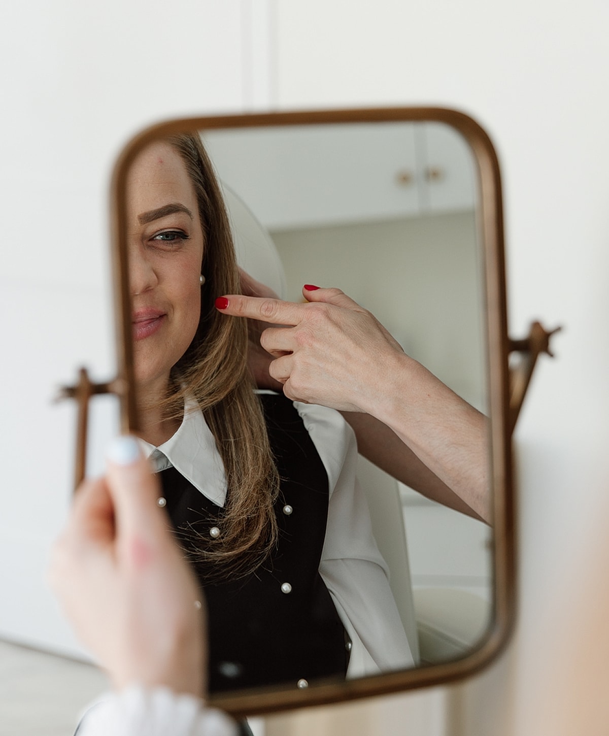 Woman applies makeup while looking in mirror.