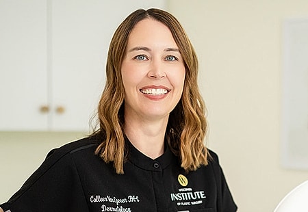 Smiling professional in medical attire, dental office setting.
