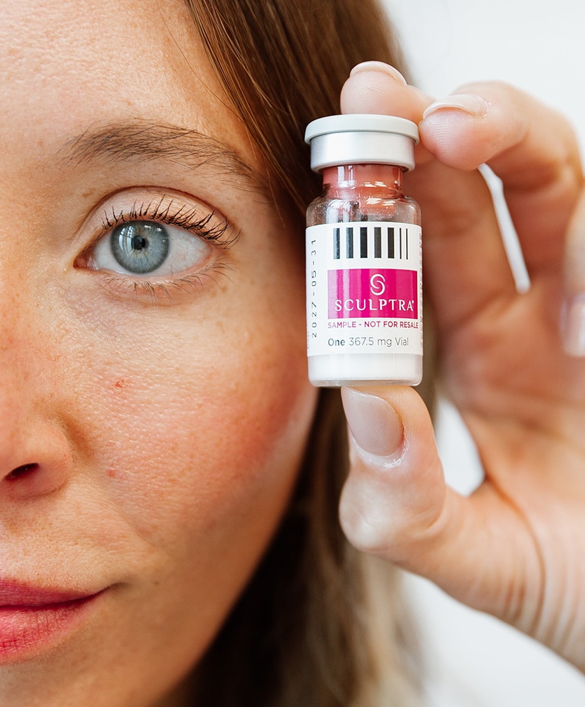Woman holding Sculptra vial near her face.