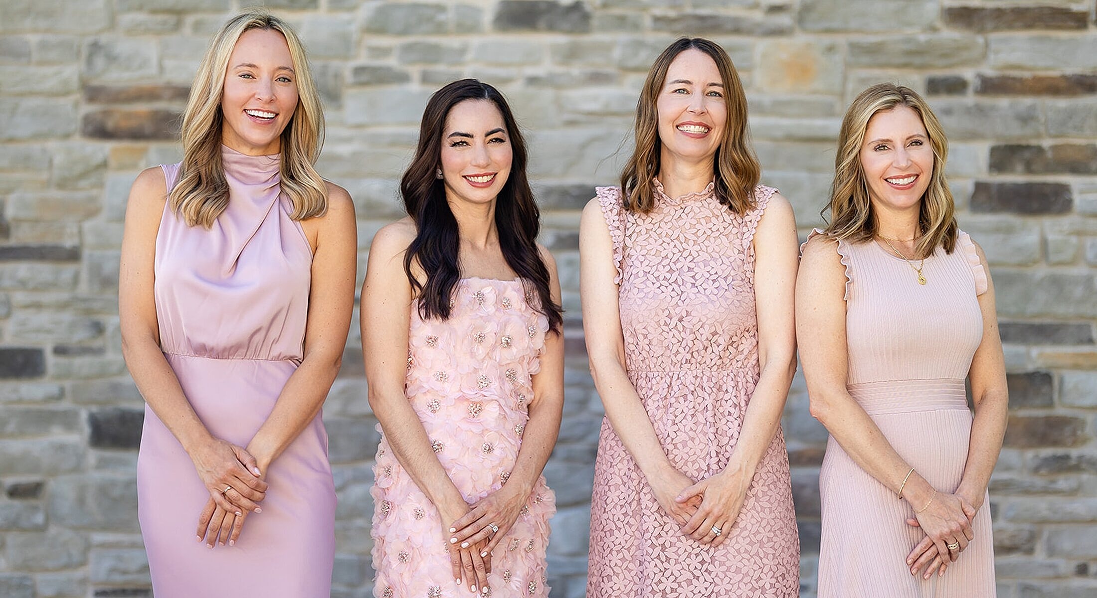 Four women in fashionable pink dresses smiling.