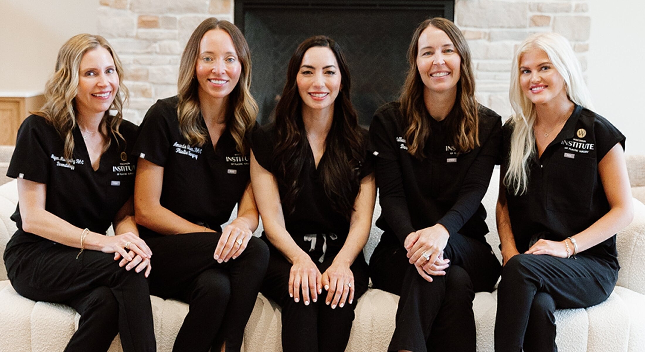Five women in black scrubs, smiling together.