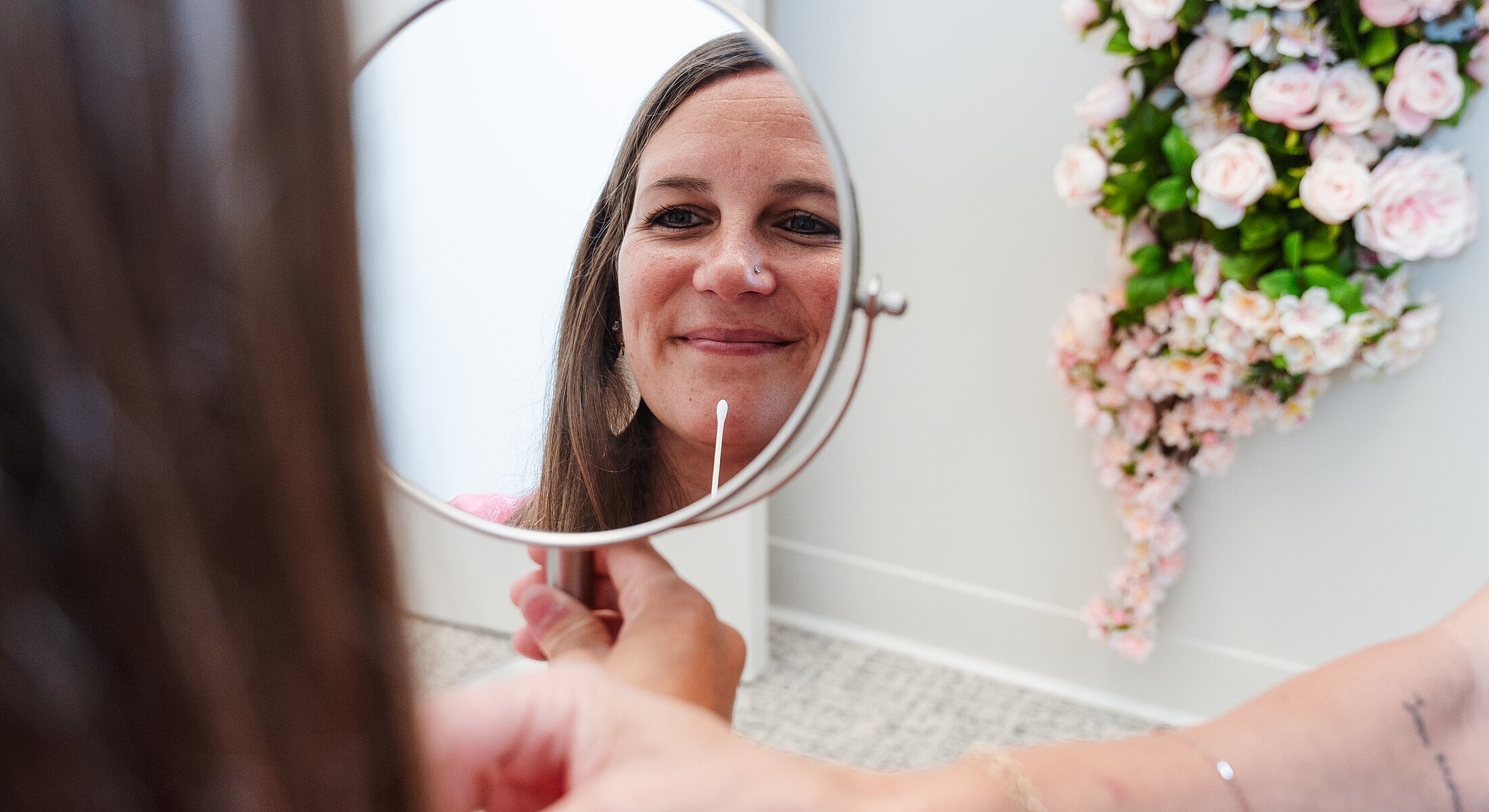 Woman looking in mirror, holding cotton swab.