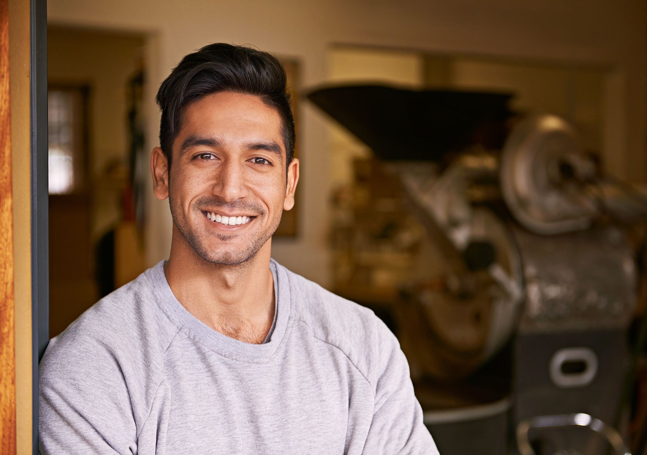 Smiling man in casual sweater, workshop background.
